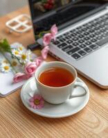 Cozy workspace with a cup of tea and fresh flowers near a laptop photo