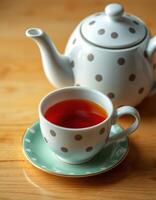 Warm tea served in a polka dot cup with a matching teapot on a wooden table photo