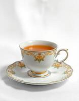 Elegant tea cup with orange liquid on a decorative saucer against a soft white background photo