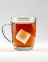 Hot tea with sugar cube dissolving in clear glass mug on plain background photo
