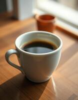 Warm coffee cup rests on a wooden table beside a small pot in a sunlit room during the morning hours photo