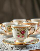 Elegant porcelain tea cups with floral designs and golden accents displayed on a lace tablecloth photo