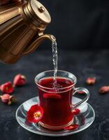 Pouring vibrant herbal tea into a glass cup adorned with red flowers photo