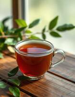 Warm cup of tea sits on a wooden table beside green leaves in a bright, natural light setting photo