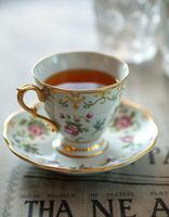 Delicate porcelain cup filled with tea on a vintage newspaper background showcasing intricate floral designs photo