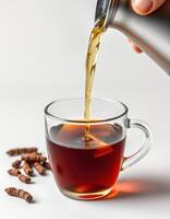 Hot beverage being poured into a glass cup with chocolate pieces nearby on a white surface in a cozy setting photo