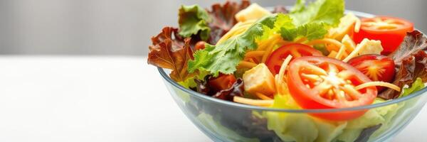 Fresh vegetable salad with tomatoes, lettuce, and cheese cubes served in a clear bowl on a white surface photo