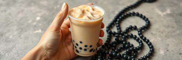 Enjoying a refreshing bubble tea with tapioca pearls and a necklace on a textured surface in a bright setting photo