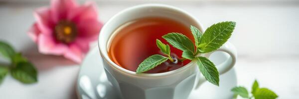 Fresh herbal tea served in a white cup with mint leaves and a pink flower on a wooden table photo