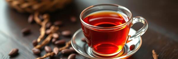 Warm tea served in a clear glass cup accompanied by cocoa beans on a wooden table photo