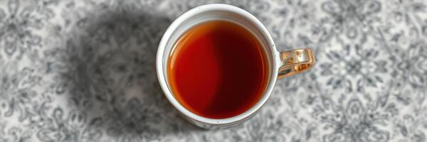 Cup of steaming tea on an elegant patterned tablecloth with warm hues and intricate designs photo