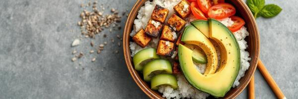 Colorful vegan rice bowl with grilled tofu, fresh vegetables, and avocado on a textured surface photo