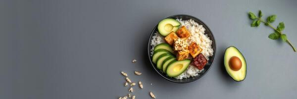 Fresh avocado and cucumber bowl with rice and tofu prepared on a plain background photo