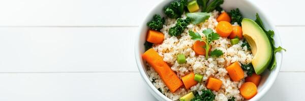 Fresh vegetable bowl with kale, carrots, and avocado served in a white dish on a light wooden surface photo