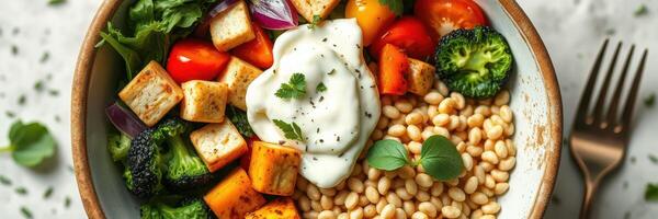 Colorful and nutritious bowl of roasted vegetables, grains, and yogurt served for lunch with a fork on the side photo