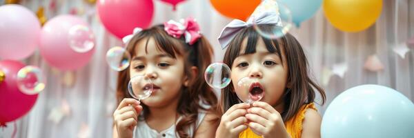 Two young girls blowing bubbles at a colorful birthday party surrounded by balloons during daytime photo