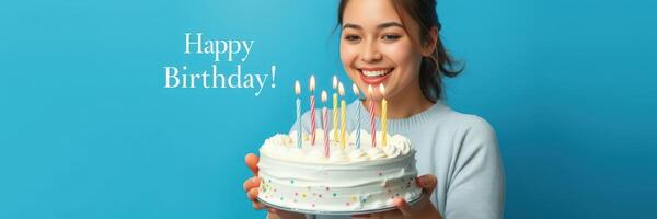 Celebration of a birthday with a joyful individual holding a colorful cake adorned with candles against a blue background photo