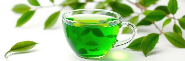 Freshly brewed green tea in a clear cup surrounded by green leaves on a white surface photo