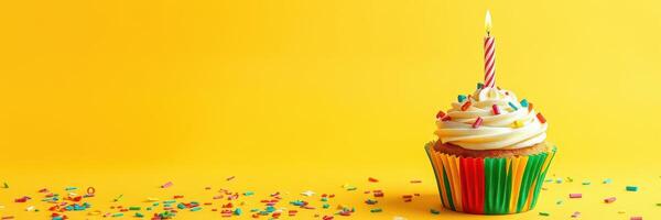 Colorful cupcake with a candle and sprinkles on a bright yellow background during a birthday celebration photo