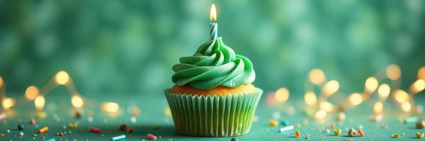 Colorful green cupcake with candle on a festive table decorated with sprinkles photo