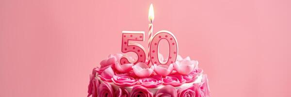 Celebration of a 50th birthday with a pink themed cake adorned with roses and a lit candle photo