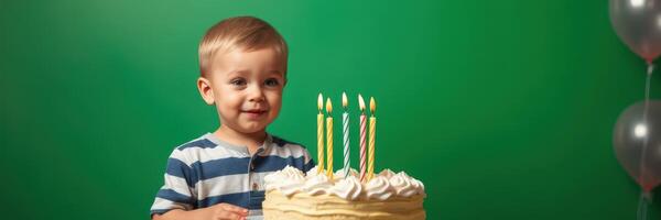 Young child celebrates birthday with cake and candles in front of green background photo