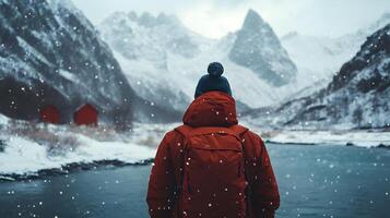 A man in a red jacket stands in the snow next to a body of water photo