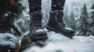 A person is standing on a rock in the snow wearing black boots photo