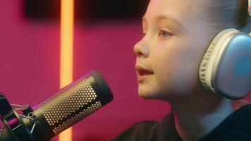 Face teenager talking microphone little girl child kid daughter gamer looking at monitor screen playing online game radio host talk online virtual computer streamer live streaming in neon light video