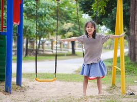 Cute girl having fun on the swing in the playground in the park. Children playing in the playground during summer vacation. photo