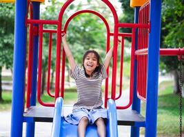 Cute girl playing in the playground during summer vacation. Happy girl having fun on a colorful slide in an outdoor park. photo