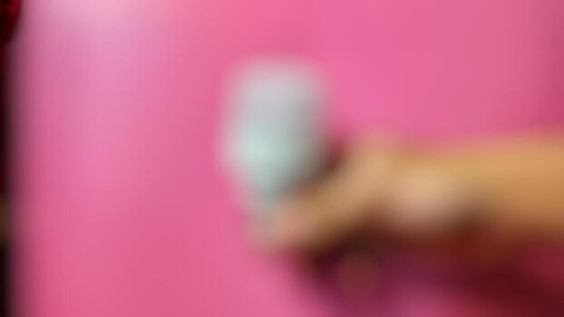 A person holding a remote control in front of a pink wall photo