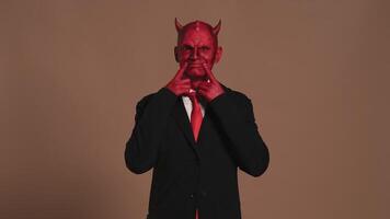 Red devil businessman forcing a smile on brown background video