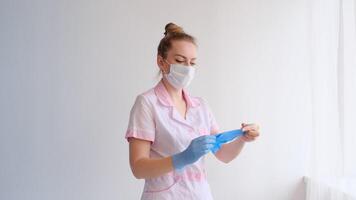 nurse in a pink uniform and a protective mask puts on gloves video