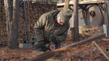 A craftsman is focused on cutting metal rail using an angle grinder in a rustic outdoor workshop. video