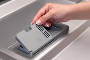 female hand puts dishwasher tablet into open automatic built-in dishwasher machine. Close up photo