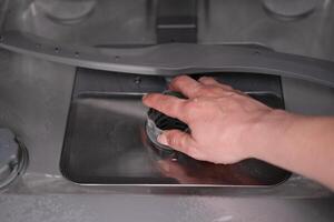 woman's hand checking the filter in the dishwasher photo