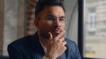 Pensive guy Arabian Indian business man thinking looking at camera close up male thoughtful puzzled businessman office think question idea solution problem search choose decide consider ponder serious photo