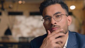 Pensive guy Arabian Indian business man thinking looking at camera close up male thoughtful puzzled businessman office think question idea solution problem search choose decide consider ponder serious photo