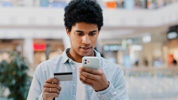 African Dominican guy doing online shopping transaction in net man with phone enters card number problems with finance error in mobile app authorization denied lack of money in bank purchase trouble photo
