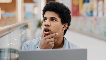 Close up pensive male african guy rubbing chin thinking solution problem plan strategy startup idea sitting with laptop indoor male writer composing novel journalist working deep in thought difficulty photo
