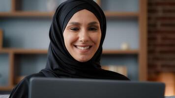 Close up Muslim Arabian Islamic woman in hijab looking at laptop screen computer monitor e-commerce buying online in internet service store typing chatting in social networks working remote browsing photo