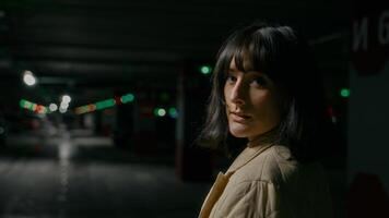 View from behind close up headshot portrait Caucasian woman female lady girl standing at dark empty dangerous parking lot turning back looking at camera with calm face scare afraid in underground photo