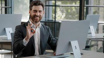 Happy success cheerful bearded 40s Caucasian adult man 30s businessman manager worker working with computer in office smile looking into camera with sign ok good idea done job approve agree advertise photo