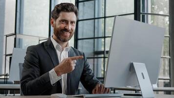 Adult Caucasian bearded businessman in office space working with online computer app website showing with index finger pointing with forefinger to screen wave head yes choice recommendation advertise photo