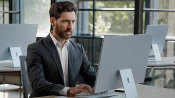 Successful adult bearded freelancer worker man at office working typing laptop smiling at camera. Portrait satisfied 40s businessman browsing laptop at workplace happy with new job in modern company photo