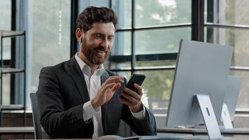Bearded middle-aged business man in office sitting table using phone mobile audio app service to listening music singing song with modern wireless headphones enjoy online radio website in smartphone photo