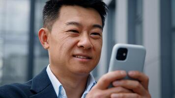 Close up male in city outdoors looking phone screen Asian 40s businessman entrepreneur employer man using mobile app map navigation in smartphone chatting browsing working distant virtual organizer photo