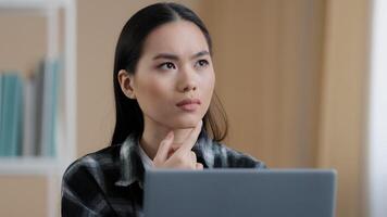 Thinking student girl asian pensive woman portrait sits in front of laptop doing online task looking for problem solution feels doubtful deep in thoughts makes decision comes up with idea find answer photo