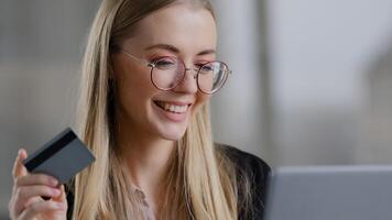 Smiling caucasian business woman shopping online using laptop paying with credit bank card buy order booking remotely net. Happy 30s female with glasses purchas website internet banking secure system photo